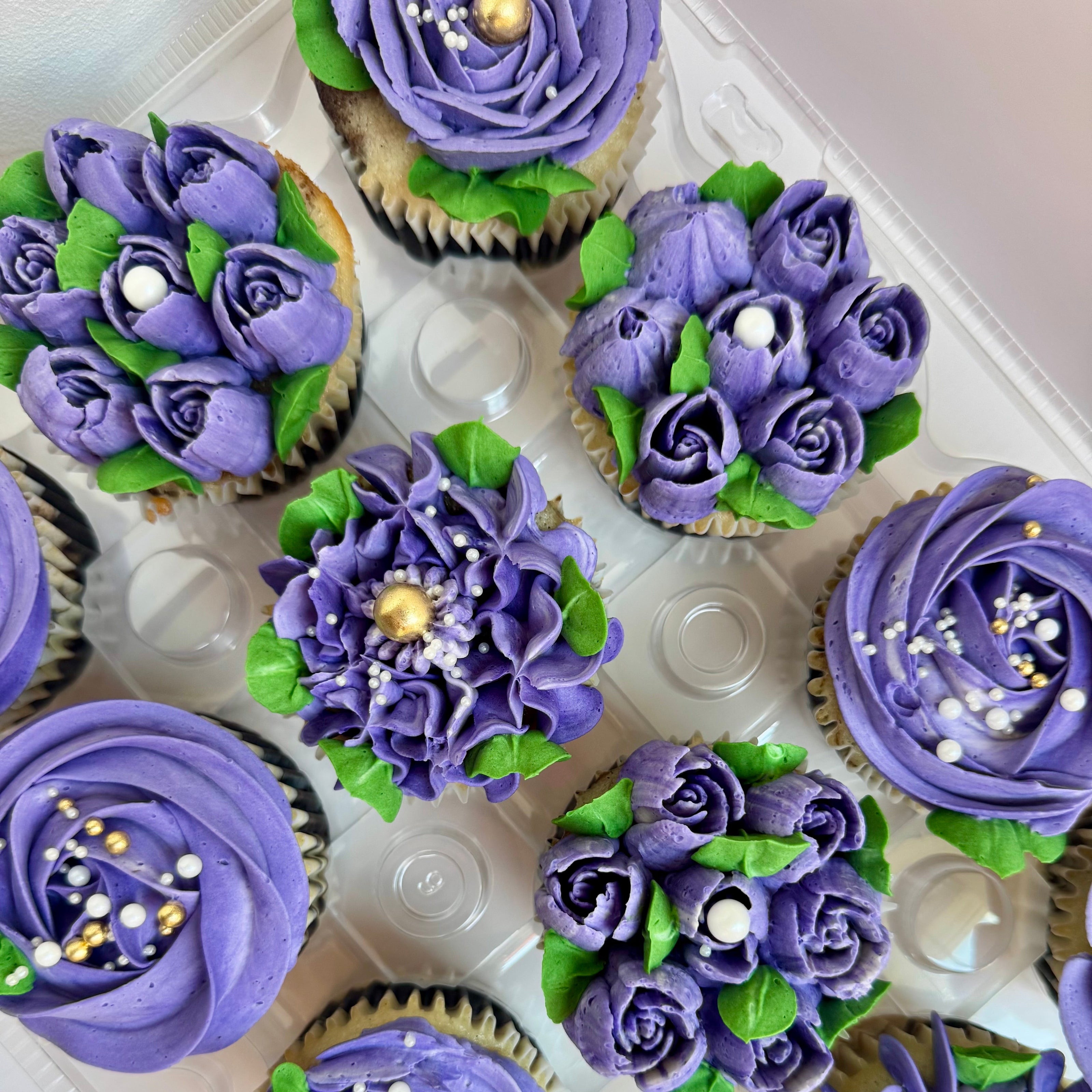 Decorative cupcakes with purple frosting and floral designs on a white tray.